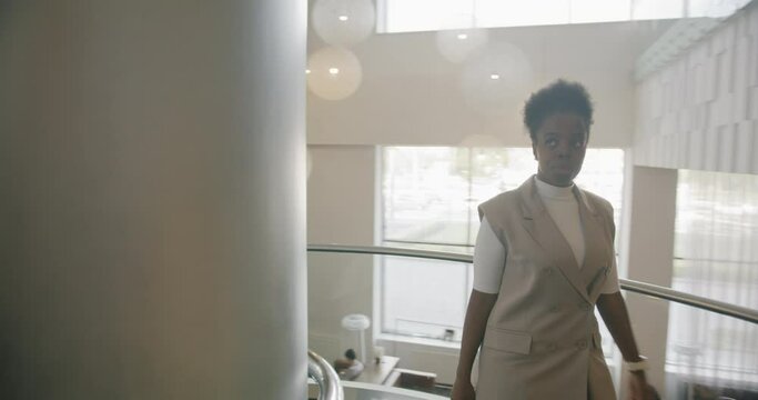 Dolly shot of joyful African American businesswoman walking upstairs in spacious luxury hotel greeting people. Commuting and corporate lifestyle concept.