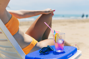 a sexy girl takes a pink cocktail close-up on the beach, a girl in a swimsuit lies on a sun lounger near the pool, close-up stands close-up of a pink cocktail.The concept of relaxing on the beach