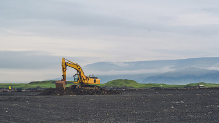 Yellow excavator on black sand against the backdrop of mountains. Construction in Iceland....