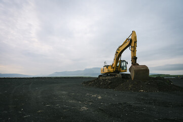 Yellow excavator on black sand against the backdrop of mountains. Construction in Iceland. Beautiful nature