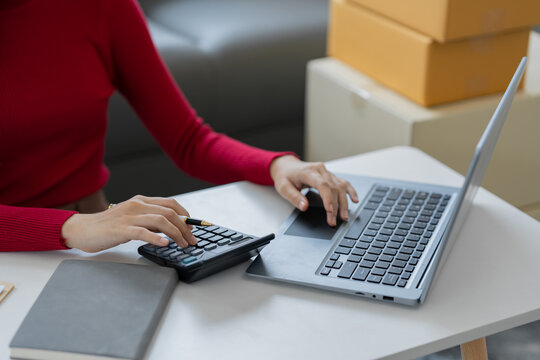 female online seller online shop use calculator and a laptop to calculate the cost before packaging e-commerce products. check online retailer orders in drop shipping.