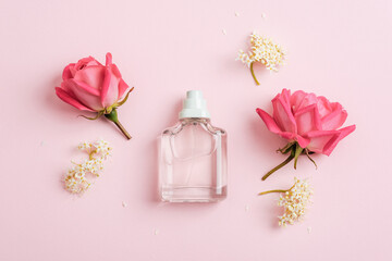 Glass perfume bottle and rose flowers on pink background. Top view, flat lay, mockup