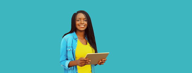 Portrait of happy smiling young african woman with tablet pc on blue background