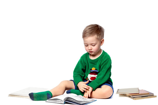 A little boy, sitting on a shelf, examines with interest the pictures in the book that was read to him.The child is isolated on white. The concept of early childhood development