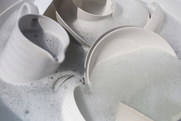 Dishes and bowls in water and bubbles of dishwashing liquid. Kitchen work