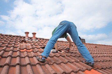 worker on the rooftop, replacing broken tiles with new shingles