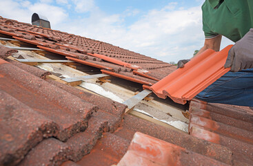 man replaces broken roof shingles on the rooftop with new ones - obrazy, fototapety, plakaty