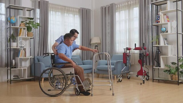 Full Body Side View Of Asian Male Nurse Helping Patient In Wheelchair Using Walker To Stand By Himself During A Physical Therapy At Home
