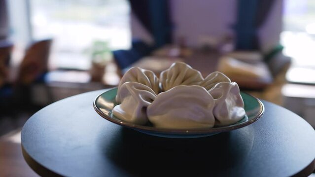 Khinkalia on a plate in the interior of a restaurant. Hot steaming khinkali dumplings lie on a white plate in a restaurant close-up. Khinkali close-up, the camera moves in a circle.