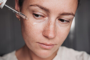 Close up portrait of a young woman applying transparent serum on her face 