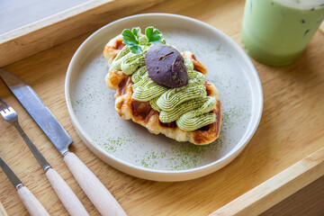 Closeup of Green tea waffles in a white plate with cutlery and cutlery set and iced green tea on a Japanese traditional wooden tray.