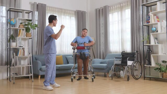 Full Body Of Asian Male Nurse Making Beckon Hand Gesture To A Patient Using Walker Walking By Himself And Raising Hand To Encourage During A Physical Therapy At Home
