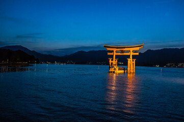 日本の広島県にある日没後の海に浮かぶ厳島神社の鳥居と小船