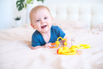 baby boy in blue bodysuit playing with colorful plastic toys on bed