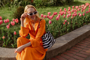 Happy smiling fashionable woman wearing stylish orange satin dress, white sunglasses, with trendy...