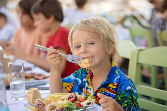 Sweet child, sitting in restaurant summertime outdoor, eating seafood, shrimps, calamari, octopus