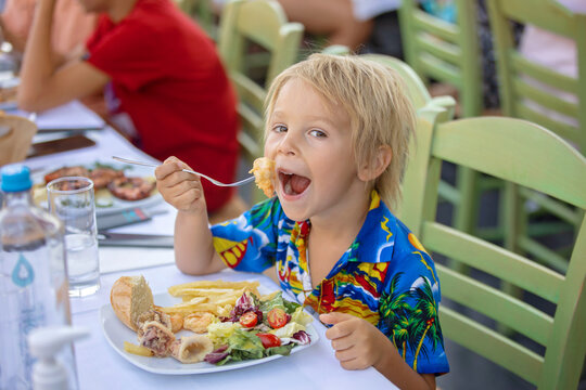 Sweet child, sitting in restaurant summertime outdoor, eating seafood, shrimps, calamari, octopus