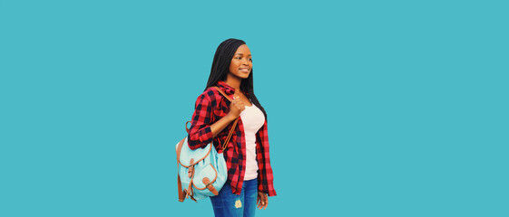 Young african woman student walks with backpack and looks away isolated on blue background
