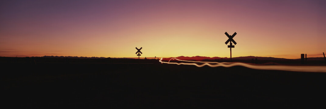 Wide-angle view of a railroad crossing at twilight with light trails from vehicle headlights; Dillon, Montana, United States of America