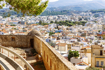 View of resort Greek architecture Rethymno city-port, built by Venetians, from height of Fortezza Castle - fortress on hill Paleokastro. Red tiled roofs and mountains in background. Crete, Greece