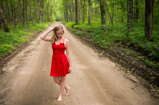 Teenage girl in red dress and barefoot on a dirt road in a wood land area; Walker, Minnesota, United States of America