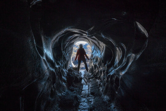View through an ice cave of a woman exploring a glacier while traveling in Iceland; Vik, South Iceland, Iceland