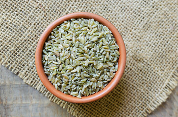 Raw freekeh or firik in ceramic bowl on burlap on wooden background. Concept of healthy food. Vegan and vegetarian food. Horizontal orientation. Top view.