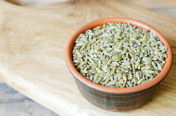 Raw freekeh or firik in a ceramic bowl with a spoon on a wooden background. Concept of healthy food. Vegan and vegetarian food. Horizontal orientation. Copy space.