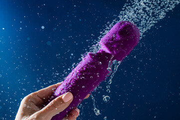 A woman washes a purple vibrator under the shower. Waterproof sex toy on a blue background.