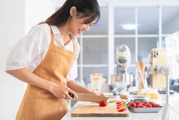 Female chef chopping strawberry , shooting video using camera on tripod. baker online courses,live stream . Healthy food vlogger in kitchen.Social media influencer. Food blogger creating content.