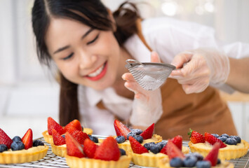 Smiling House wife wearing apron making finishing touches on birthday dessert fruit tart.Woman...