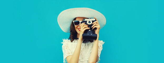 Summer portrait of happy young woman photographer with film camera wearing white straw hat on blue background