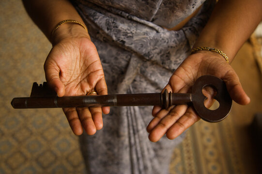 Woman holds out the large key to a mansion; Chettinad, Tamil Nadu, India