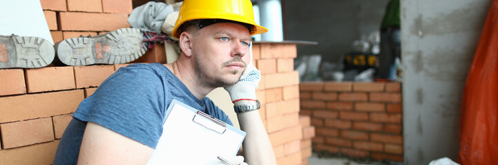 Thoughtful sad builder holding clipboard and looking into distance. Solving construction problem...