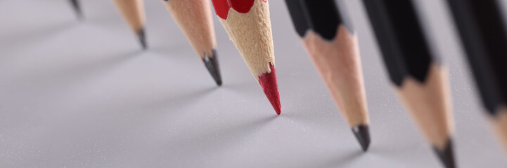 Sharp red pencil stands out from identical black pencils on gray background. Independent thinking...