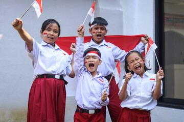Group of cheerful elemen'tary students wearing uniform school holding Indonesian flags to celebrating Indonesia Independence Day