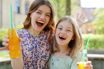 Happy woman and little girl with soda in their hands on a summer day.