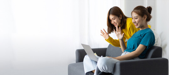 Happy asian woman and friend looking at laptop in living room at home.