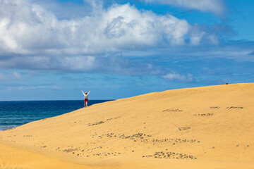 Maspalomas, eine Frau auf den Dünen von auf der kanarischen Insel Gran Canaria, blauer Himmel und Wolken im Hintergrund.