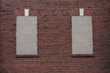 two windows sealed with cinderblocks on a red brick wall, with a decorative brick window head lintel in form of a flat gauged arch with marble keystone, copy space