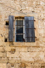 Vertical photography of old window with broken wooden shutters on an old cracked stone wall.	
