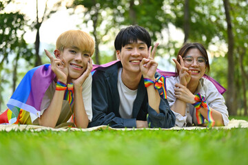 Pictured with a group of LGBT teenagers lying on the lawn, covered with rainbow flags and wearing a rainbow wristband, freedom concept, Celebration Pride month in June.