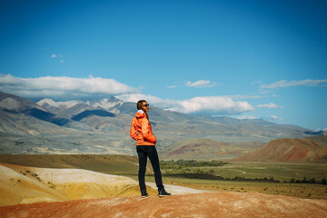 Happy young woman standing on a rock with a beautiful view. Cheerful female traveller admires stunning mountains panorama.