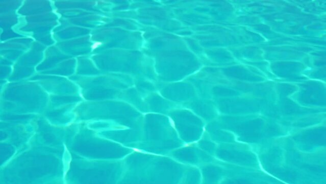 Clear Turquoise Water in a Swimming Pool Sea Ocean in Sunlight, Iridescent Glittering Water Surface in Sunbeams on a Sunny Summer Day. Abstract Blue Green Clear Water Background. Travel, Vacation.