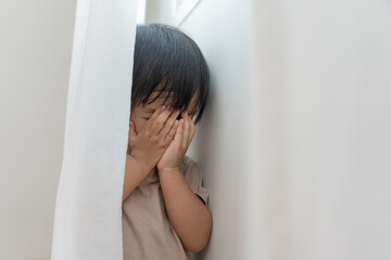 little asian children kid girl covering his eyes with hands, playing hide and seek standing next a wall house, Adorable child having fun in the home. happy family have fun with kids, activity