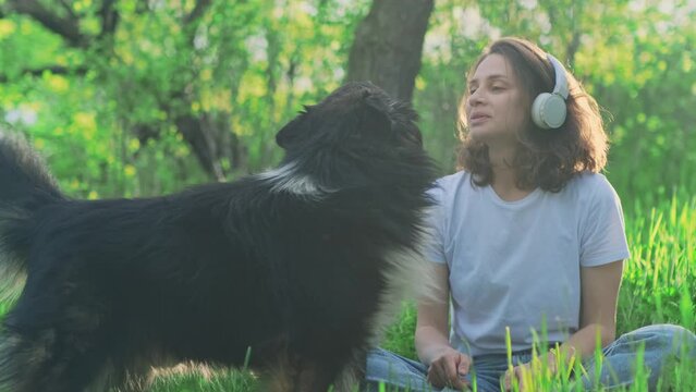 Happy young woman and her pet outdoor. Loving female owner sitting on a green lawn and playing with her big fluffy dog while walking in the summer garden.