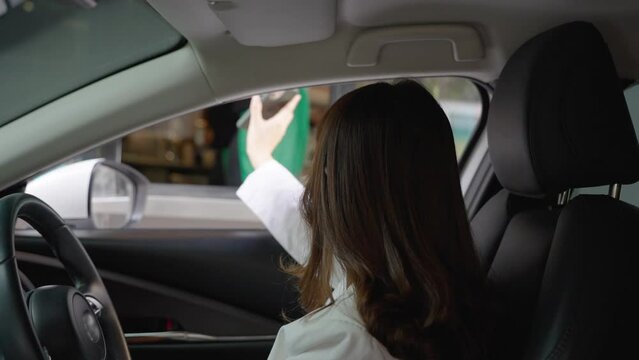 Beautiful Asian woman pay for food or beverage via e-wallet on smartphone using barcode reader qr code by driving through or drive thru. Contract less payment.