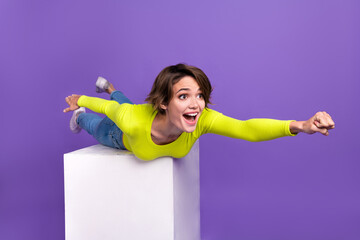 Full length portrait of overjoyed nice supergirl raise hand forward flying empty space podium isolated on purple color background