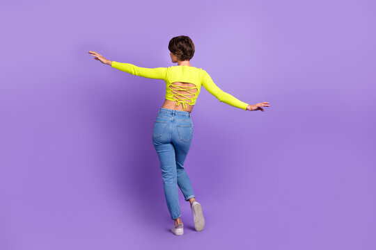 Full body cadre of relaxed flying slim woman bob hair wearing stylish crop top open spine with jeans isolated on purple color background
