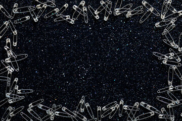 Safety pins on black felt with colored glitter. Sewing texture background
